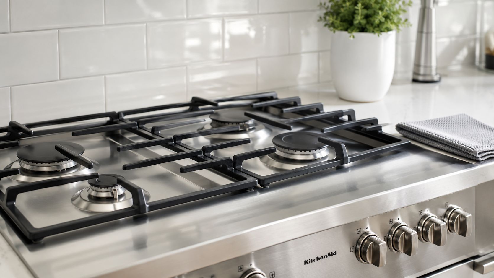 A clean stainless steel KitchenAid gas range stove top with black iron grates in a modern kitchen.