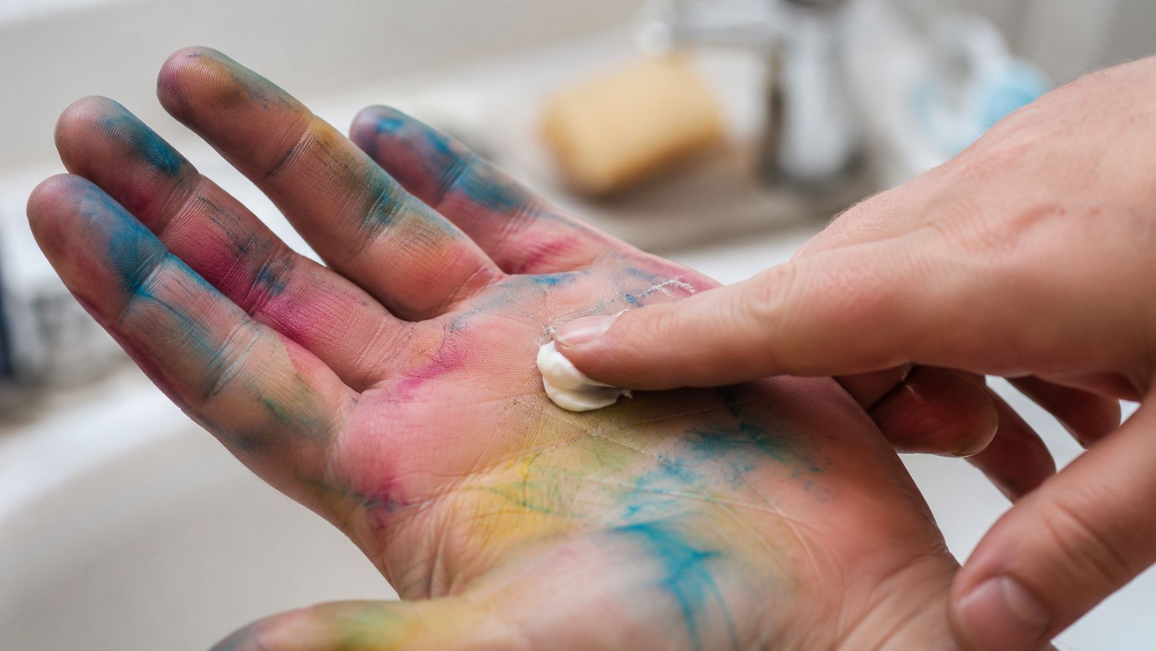 A person cleaning colorful Easter egg dye from their skin using a dollop of white hand cream.